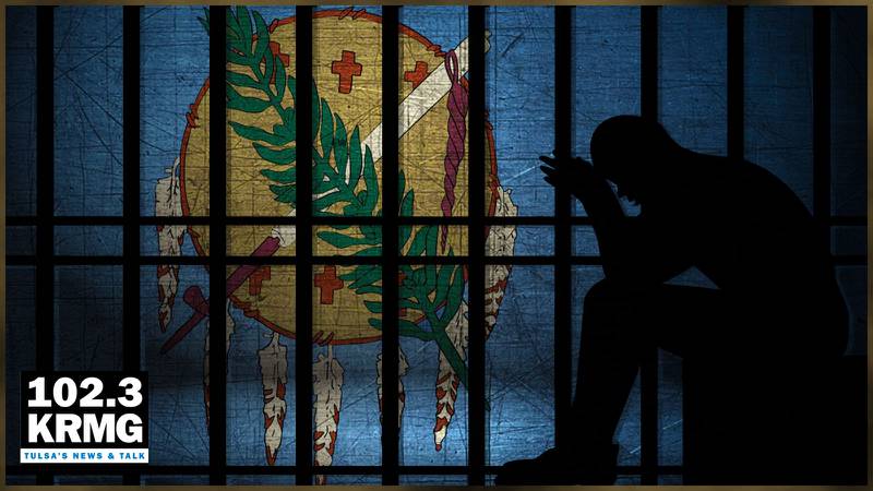 Silhouette of a man sitting inside a prison cell with an Oklahoma state flag background