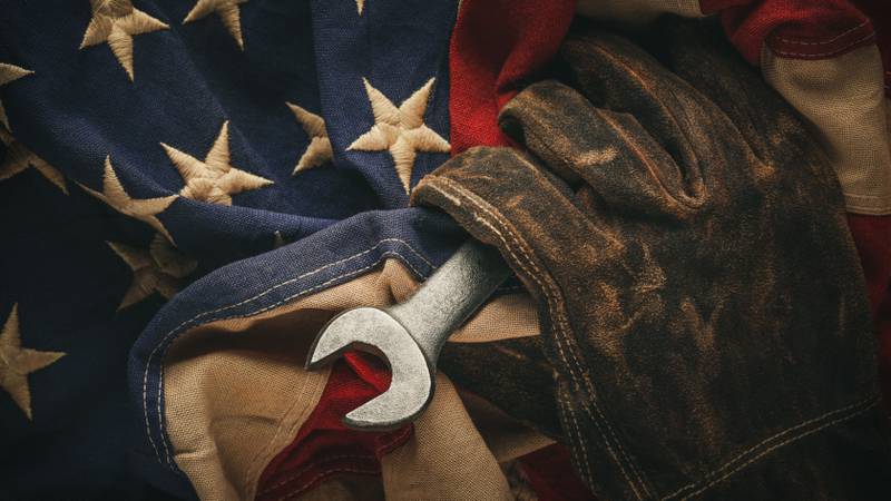 Worn work glove holding old wrench and US American flag. Made in USA, American workforce, blue collar worker, or Labor Day concept.