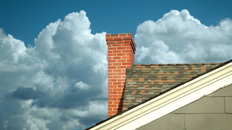 Chimney and roof with blue sky and clouds behind.