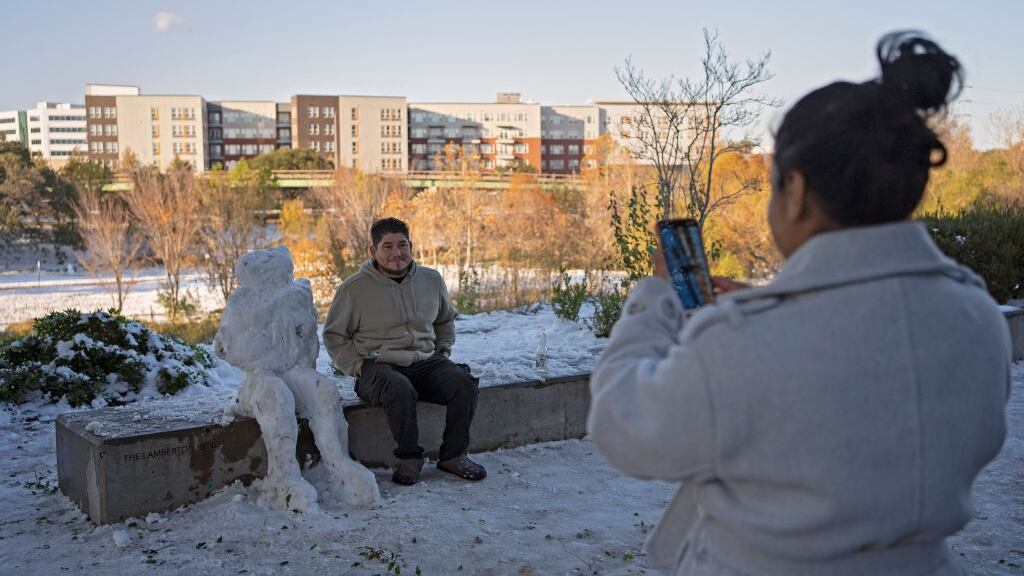 A woman takes a photo of a man amid a snow fall that was rare for Texas.
